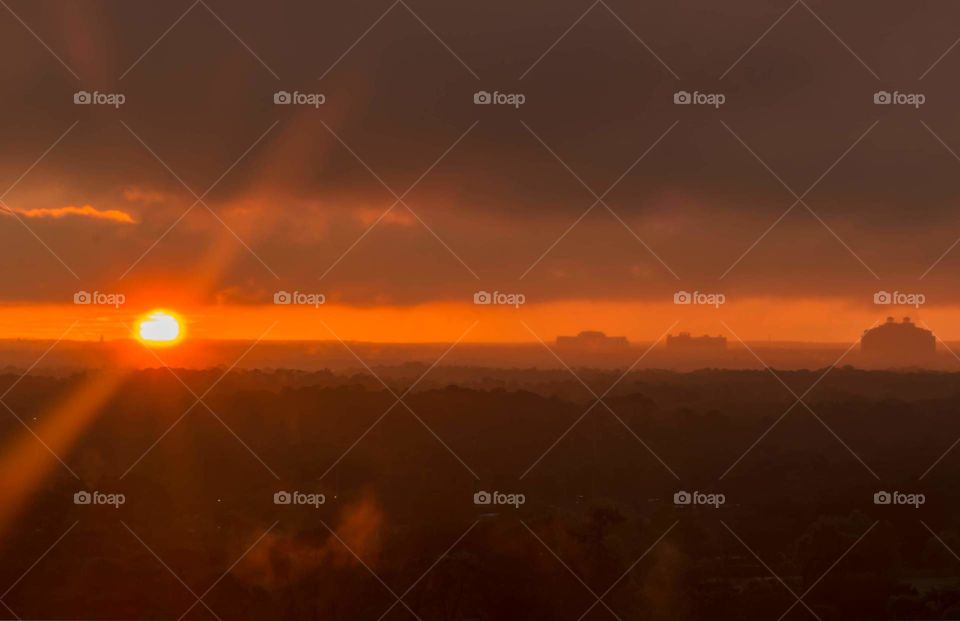 all red image of horizon line with sun setting over large field creating a red haze and a red sky with bright red sun rays