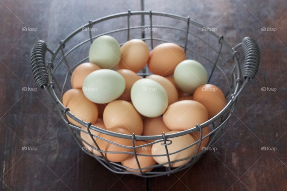 Farm-fresh blue and brown eggs in a wire basket on a dark wooden surface