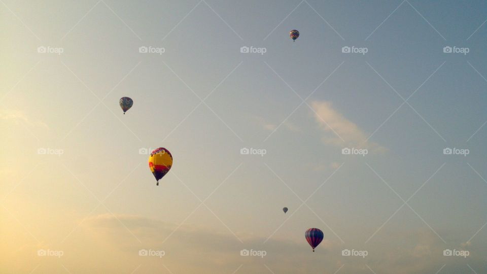 Hot air balloons flying through the sky during a setting sun. The sun is getting ready to set upon the horizon. 
