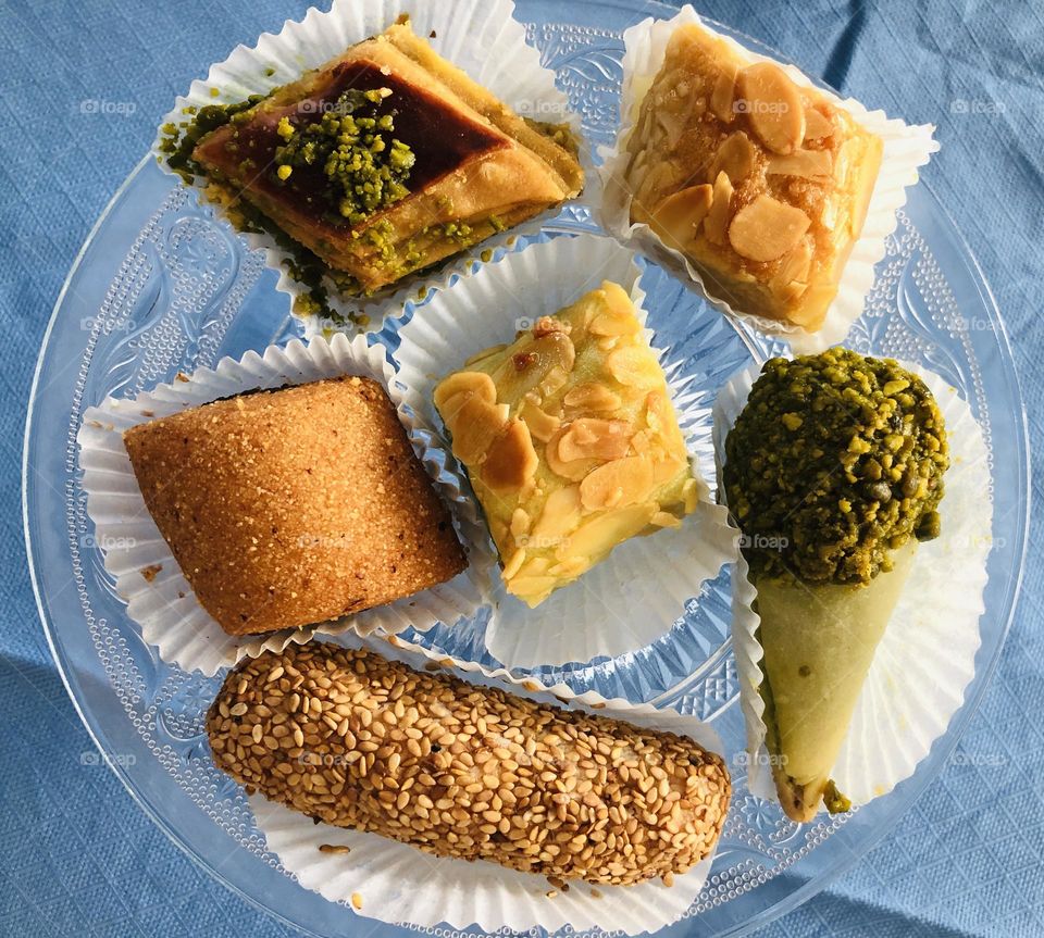 Assorted Maroccan pastries desserts on transparent dish against blue background, ethnic cuisine, ethnic patisserie