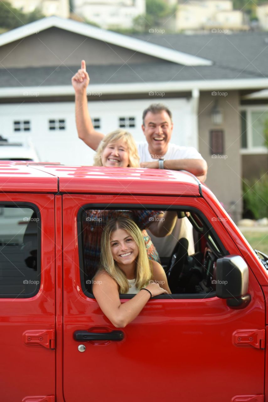 Three people going on a road trip. Excitement and happiness leaving in a red Jeep. 