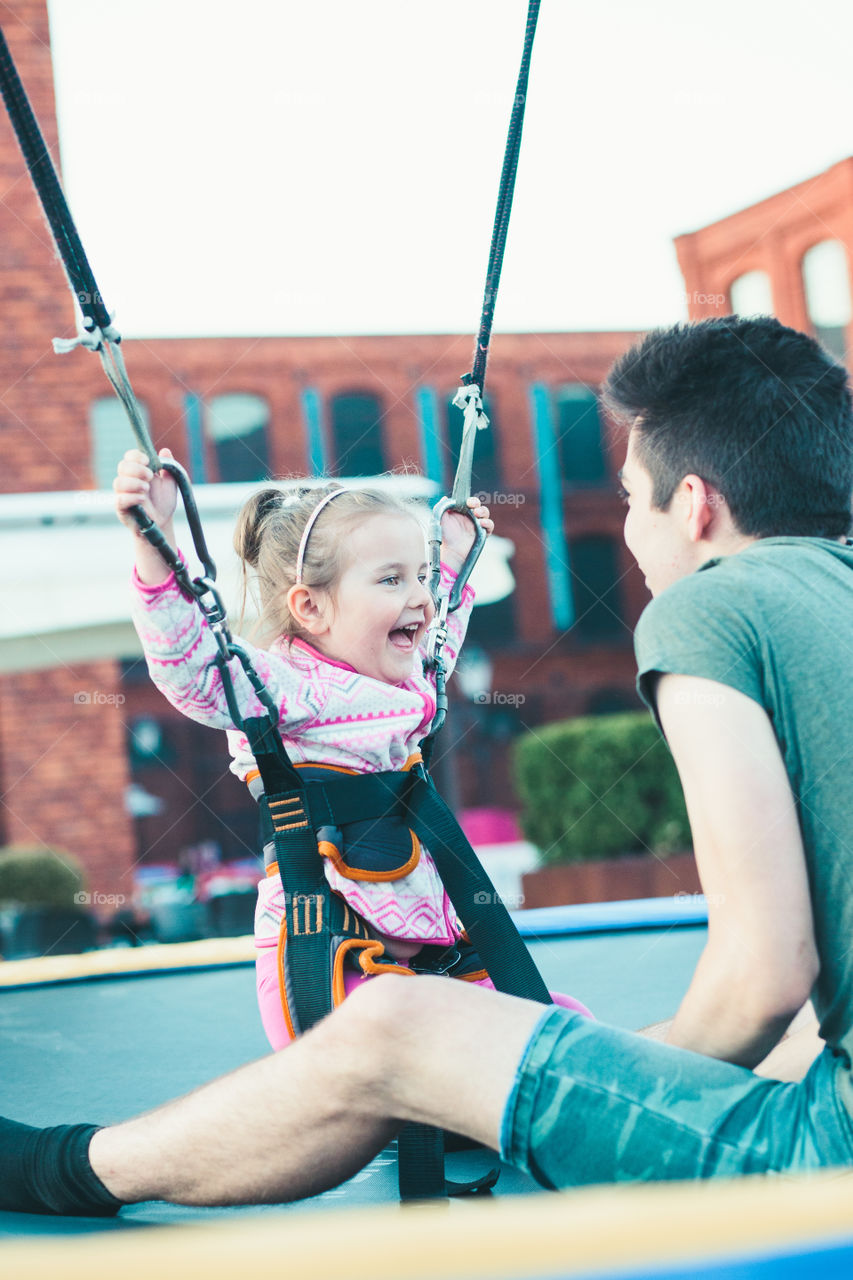 Little adorable smiling girl jumping on trampoline, having fun with her brother at funfair