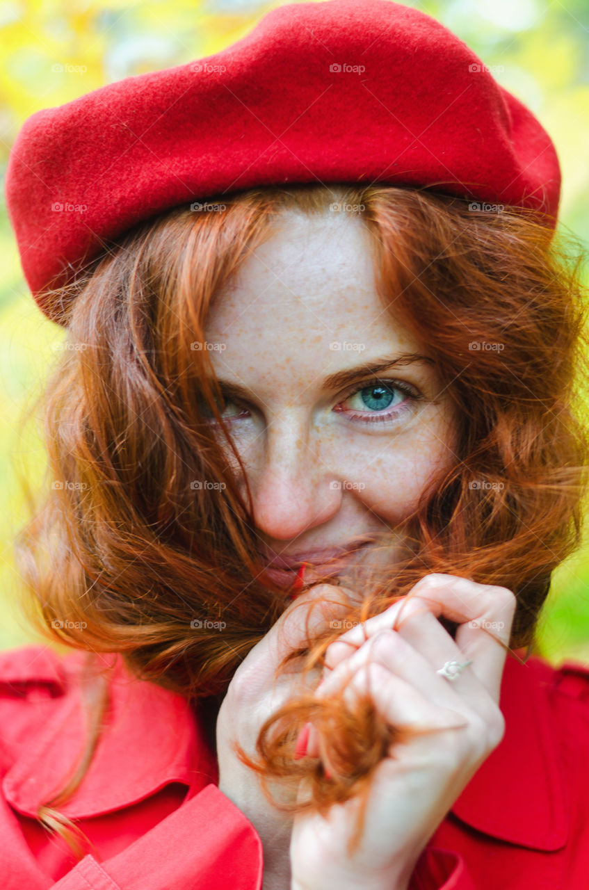 Portrait of a young redhead curly woman in red coat with freckles and blue eyes walking in autumn park. Happy people.