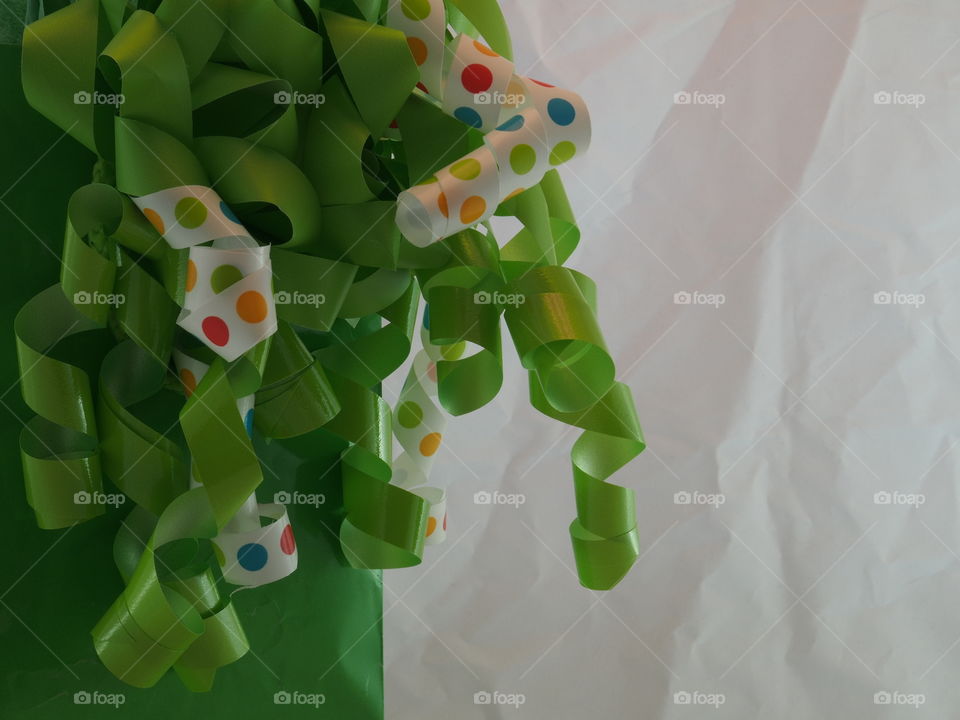 A couple of white ribbons with poke-a-dots amongst green ribbon attached to a green bag with lots of textured white space. 
