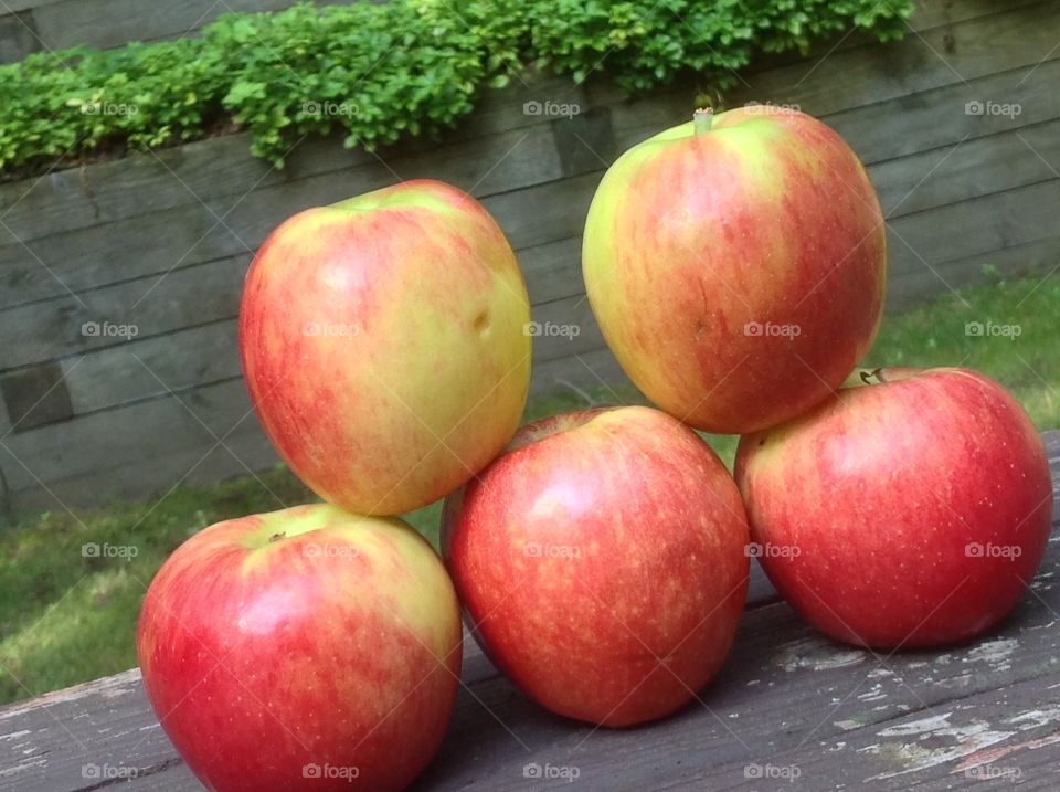 Apples stacked outdoors on wooden bench.