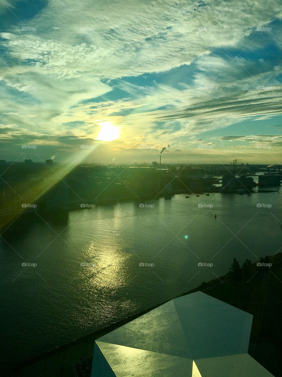 Magical sunset with sun rays going over the water behind Amsterdam central station. View from top 