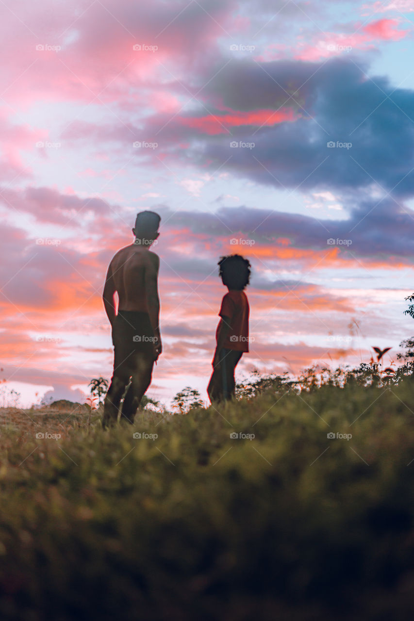 Two brothers enjoying a beautiful sunset in the middle of nature in time of social estating