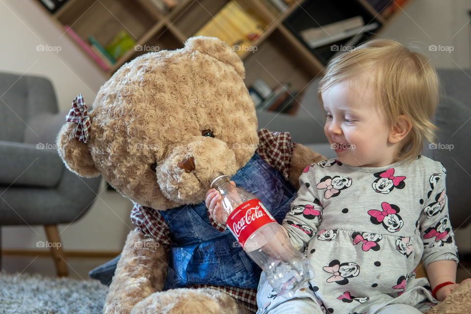 Baby girl drinking last drops of coca cola with teddy bear