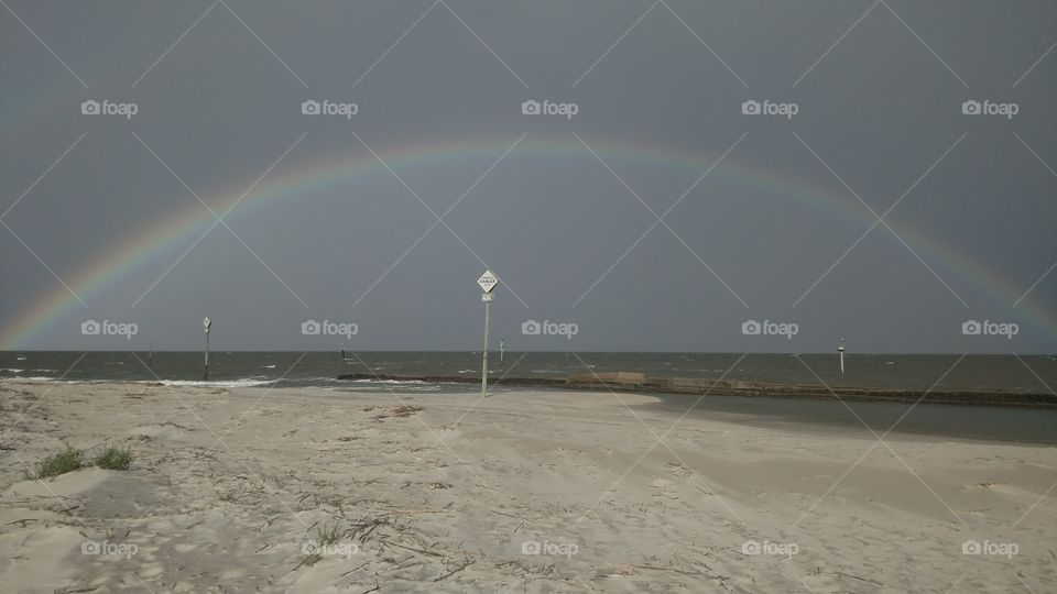 A full rainbow streches over the beach.