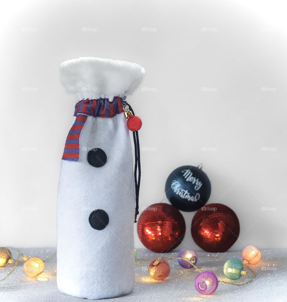 A bottled of wine in a snowman themed gift bag, with lights and baubles