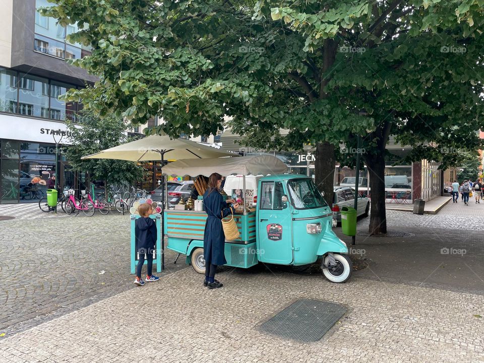 A mother buying ice cream for her kid from a turquoise ice-cream truck in the streets of Prague, Czech Republic