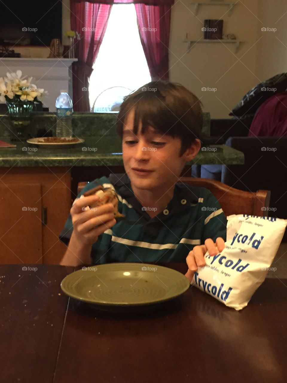 Young boy looking with a boo boo and a frozen ice pack at the kitchen table.