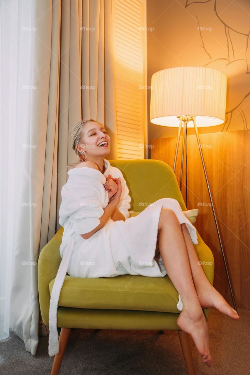 Happy, smiling blonde girl, sitting on a chair in a white bathrobe