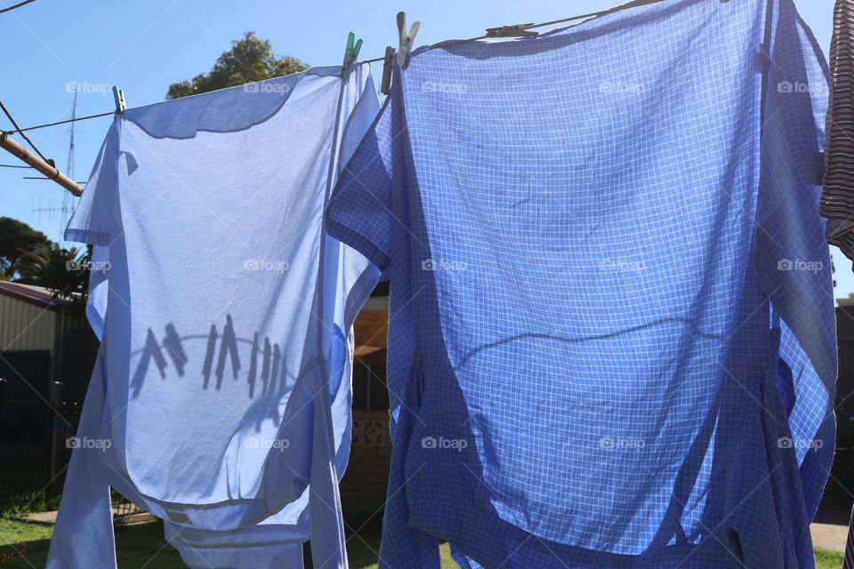 Two blue men’s shirts hanging on clothesline outdoors in backyard to dry on sunny breezy day