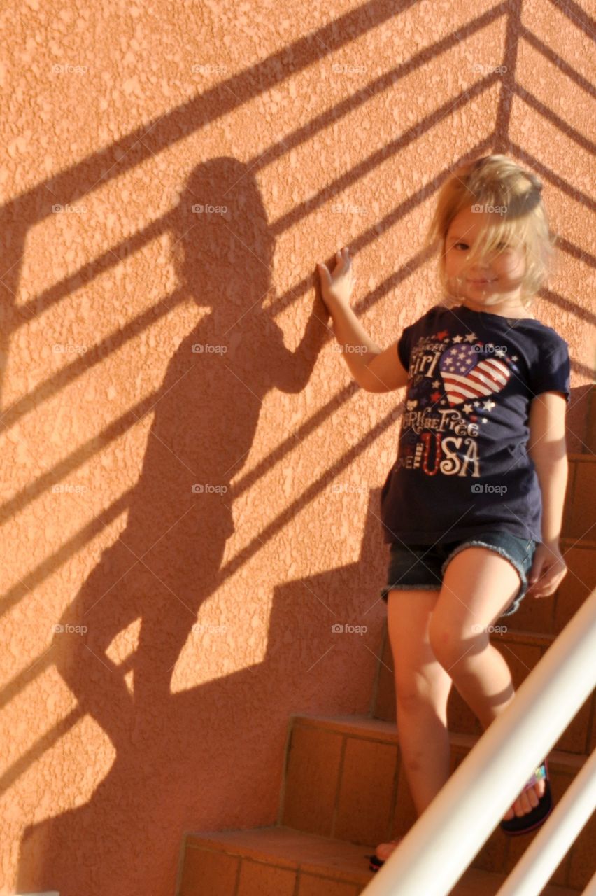 Little girl going down the steps and casting her shadow on the wall