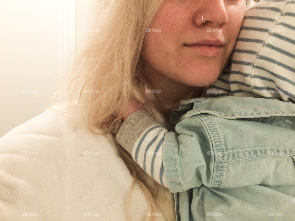 A young blonde mother with nose ring holds sleepy baby in a stripped hoody and denim T-shirt. 