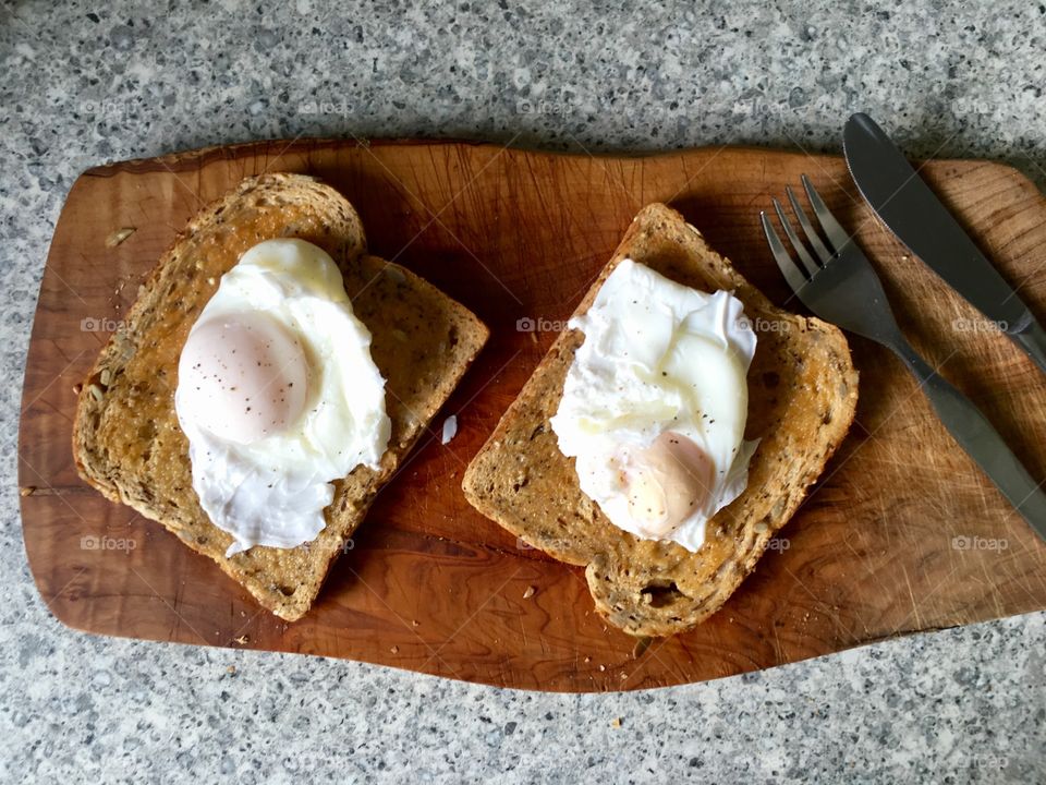 Poached eggs on toast on olive wood with cutlery 