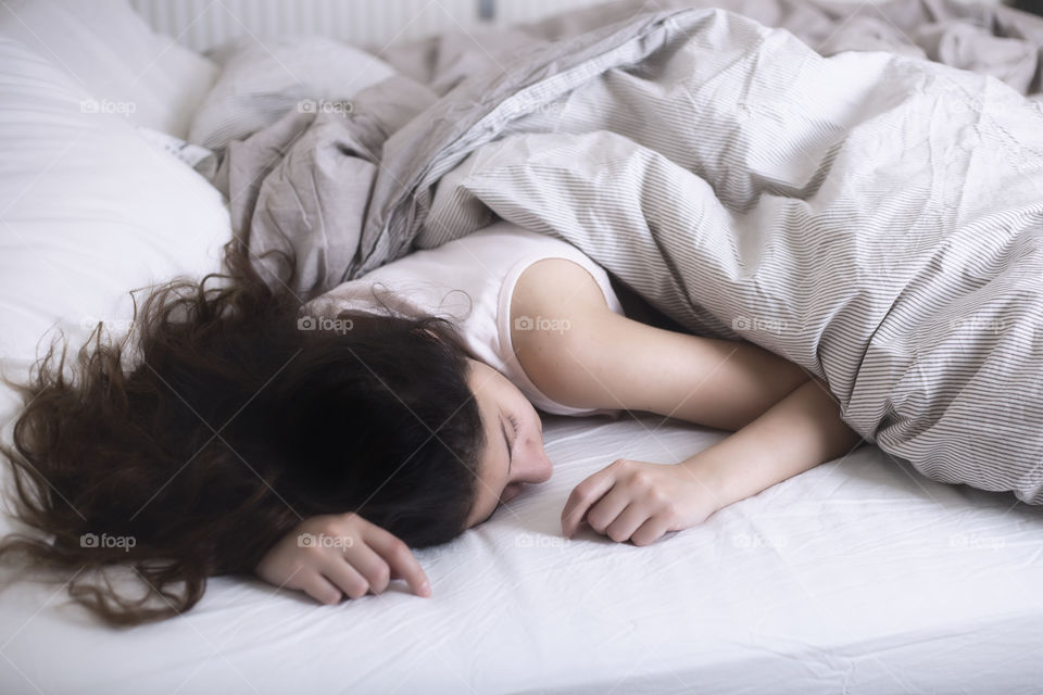 A lady sleeping under a white blanket 