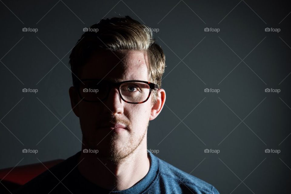 Moody shot of a young man wearing glasses and looking to the camera.