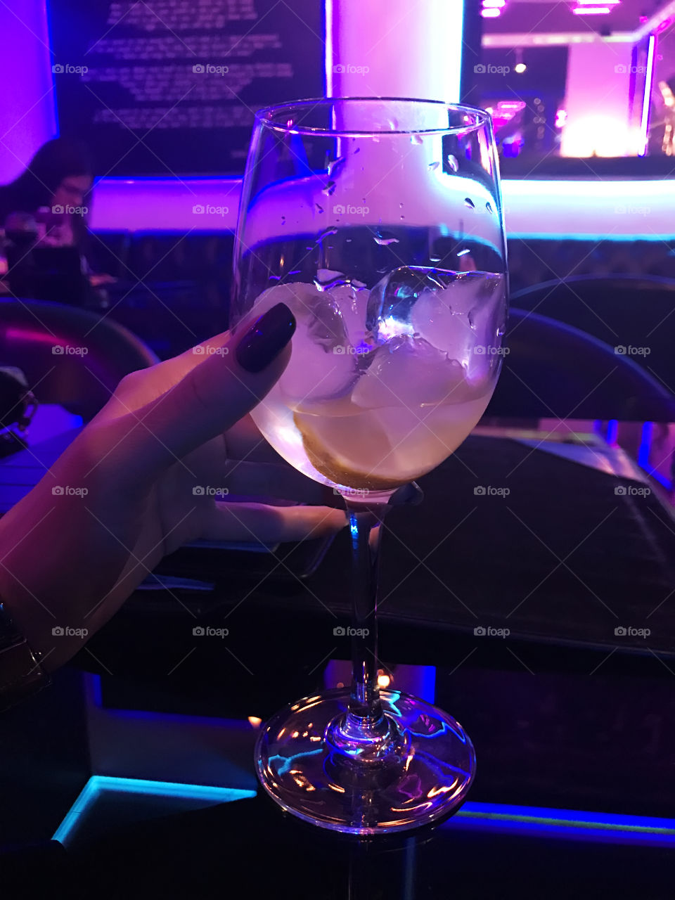 Female hand holding a glass with icee refreshing cocktail in neon light 