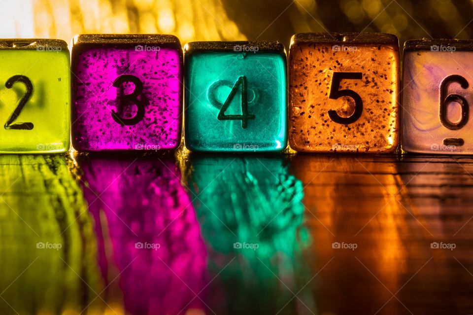 Closeup of some colorful translucent dice on a polished hardwood table revealing beautifully distorted reflections. 