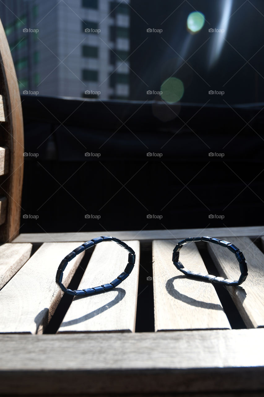 Magnetic bracelets sit on a wooden rooftop chair in the high sun of Denver, Colorado.