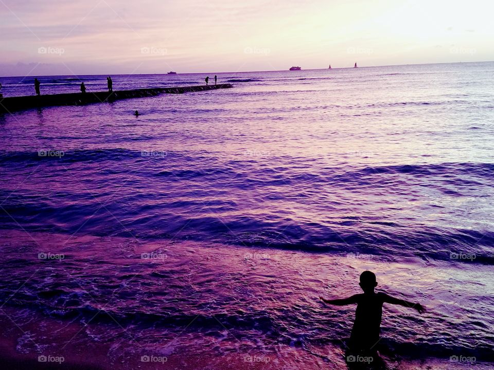 boy frolics on the seashore during sunset at Waikiki Beach