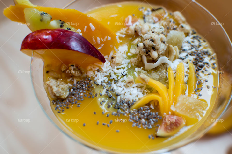 Yellow fruit smoothie in bowl with mango, ginger, peach, coconut , oatmeal, chia seed,  dried ginger,  kiwi and fig high angle view close-up detail full frame food photography 