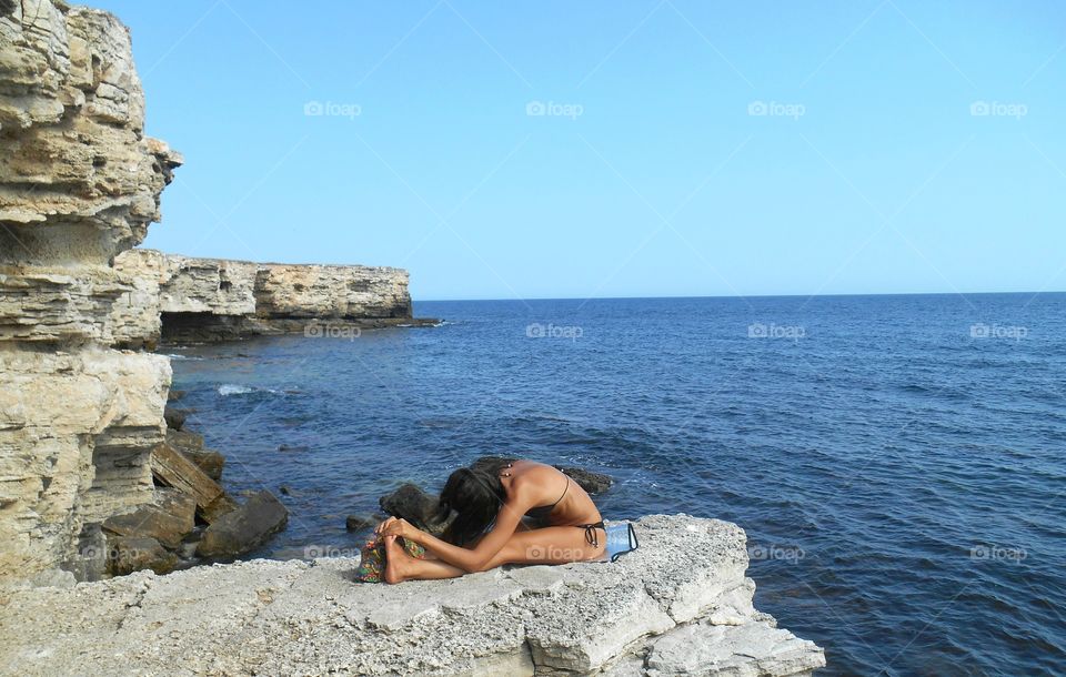 girl training yoga on a sea stone shore summer time