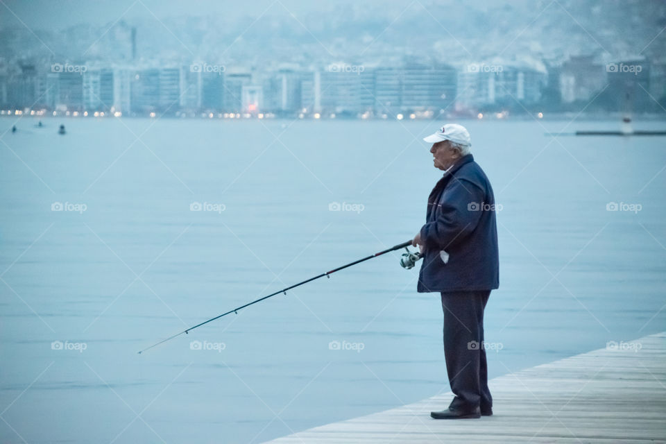 Old Man Fisherman Fishing At The City Port
