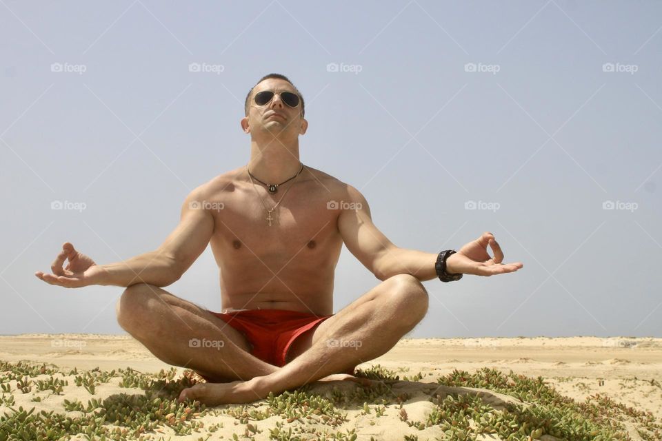 A young man is sitting on sand and meditating