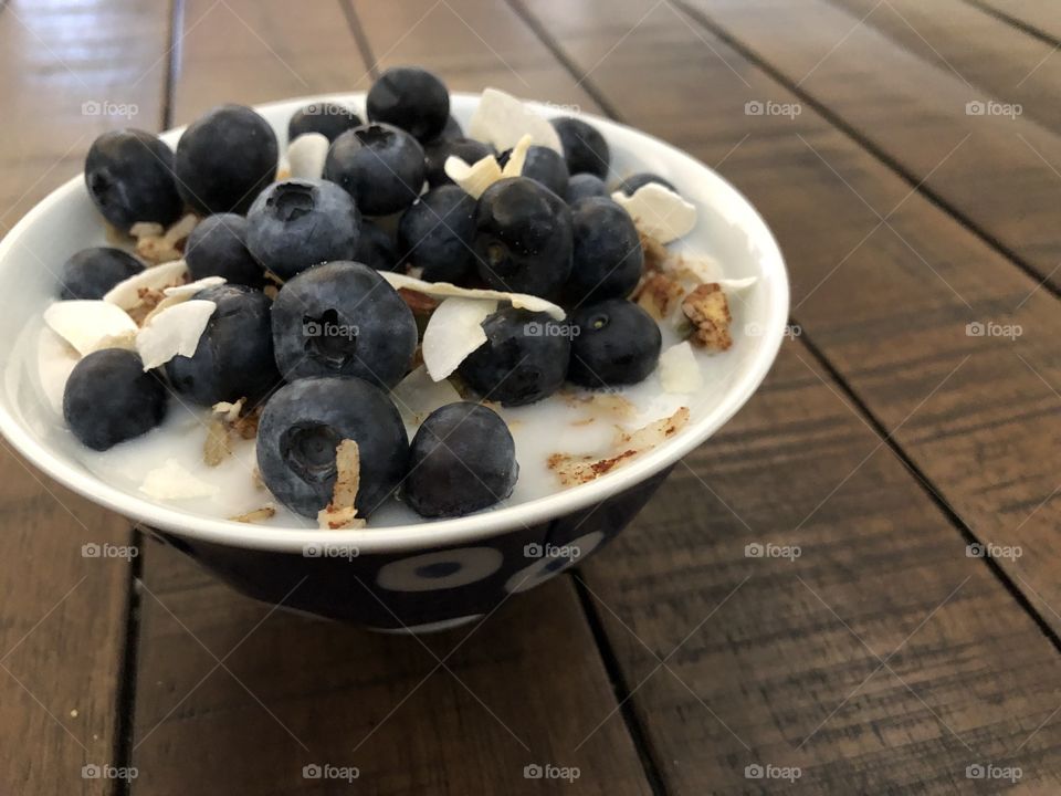 Blueberries on a bowl of coconut granola with almond milk.