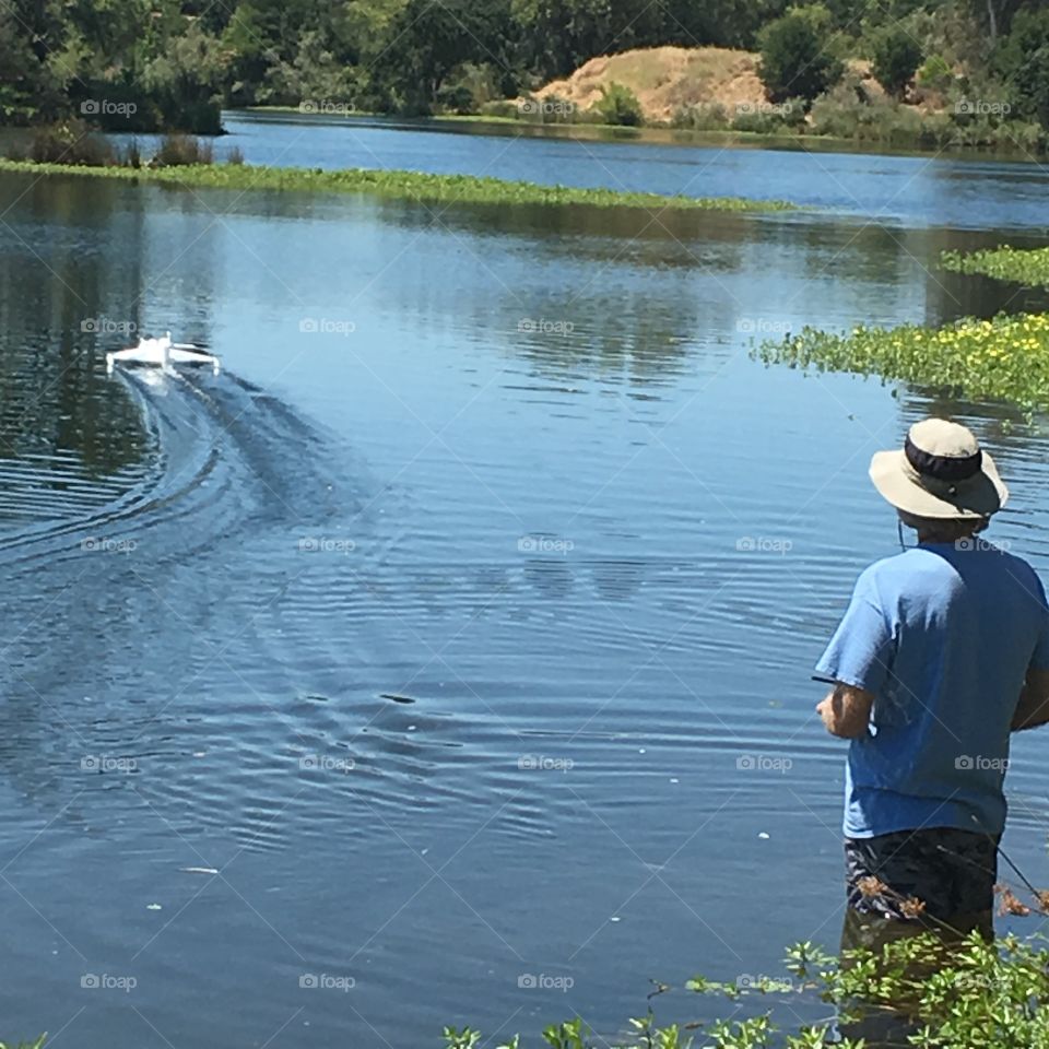 Man in water river lake marsh operating a remote control boat watercraft 