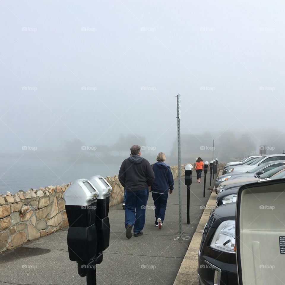 People walking to see The Mayflower in Plymouth MA USA.  Dense fog, ocean on left side.