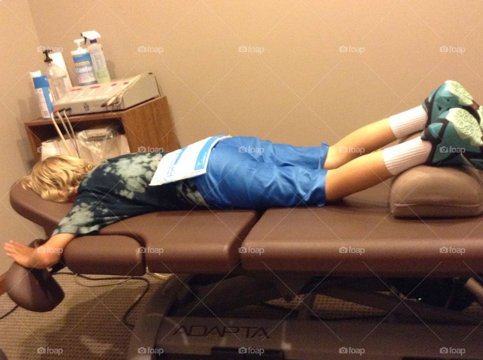 This boy is laying down in the exam room of the chiropractor's office.