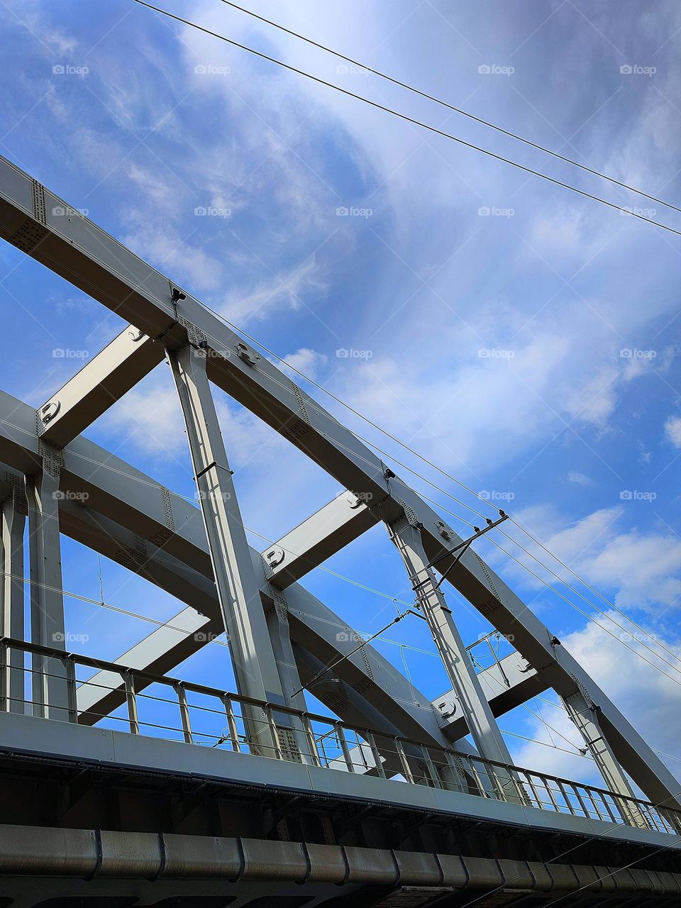 Human and nature.  Bridge geometry and cloud geometry.  View of a part of a metal bridge against a blue sky with white clouds