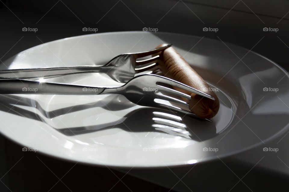 One sausage and two forks on a white porcelain plate.
