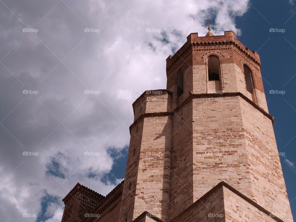 Spanish gothic church with red stones and blue decorations, blue sky and white clouds.