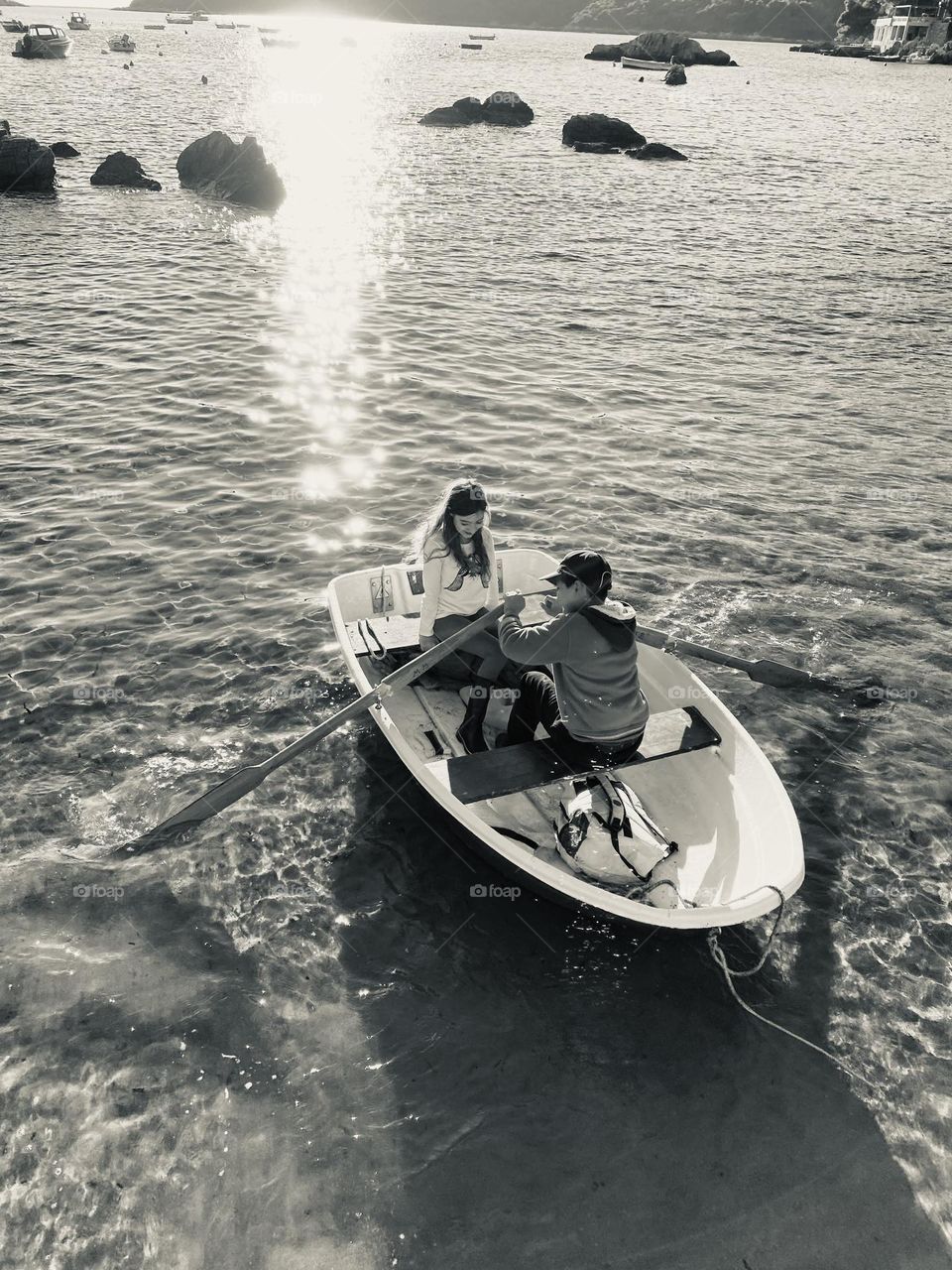 Black and white photo of a boy and girl in a rowboat with the sun glistening on the water.