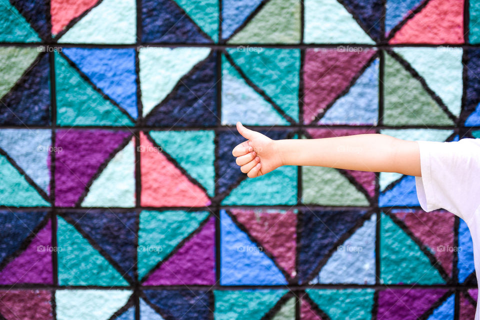 Person's arm coming into frame giving a thumbs up against a colorful patterned wall