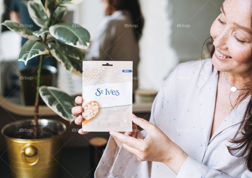 Adult woman with sheet mask in hands in bathroom at home 