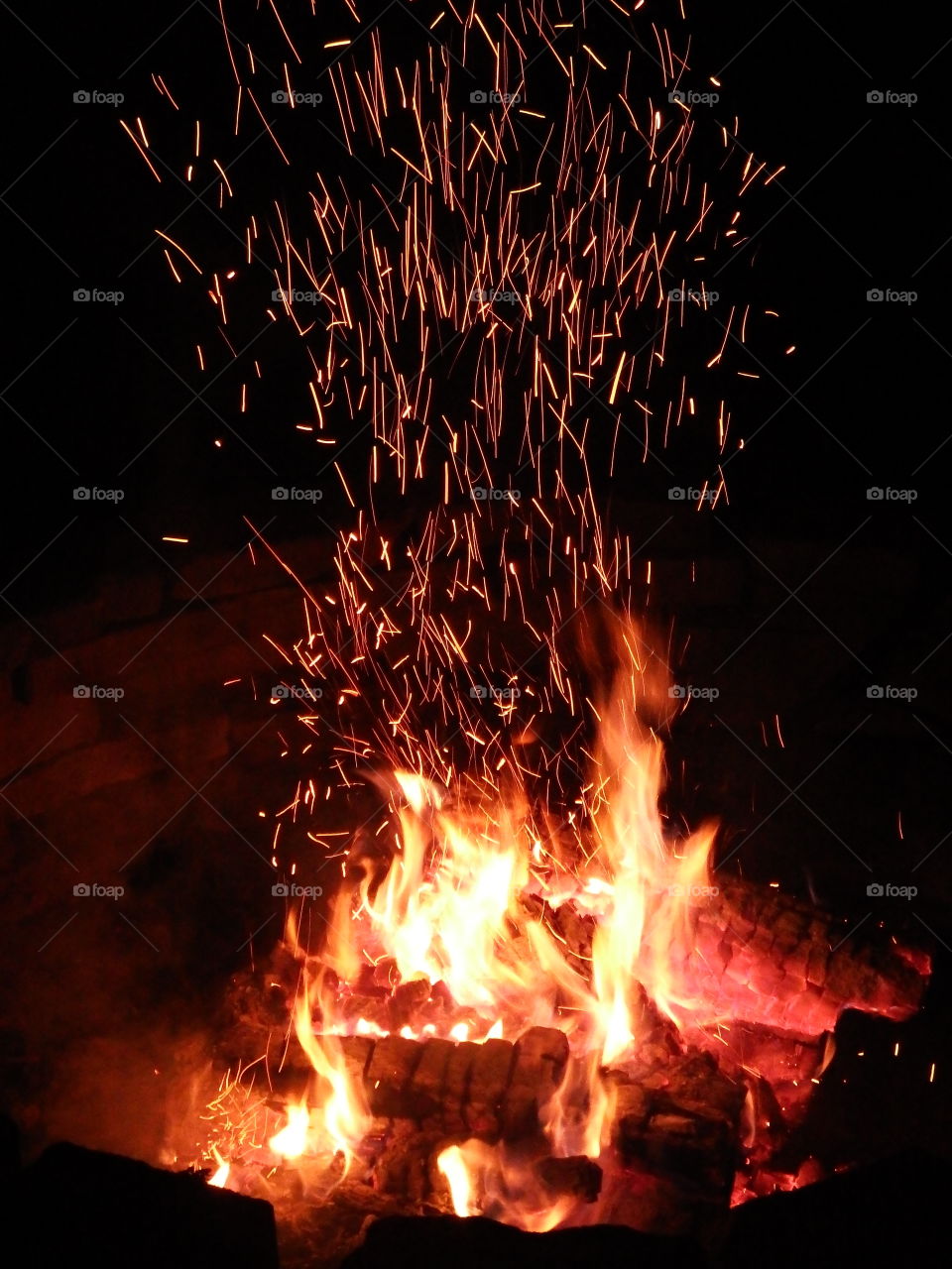 Camp fire at night stirred up with a shower of sparks shooting up.