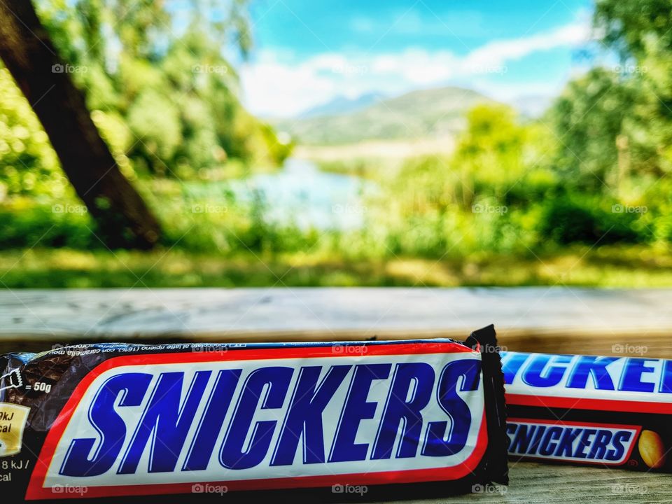 Snickers chocolate and caramel bar resting on the park bench and surrounded by nature