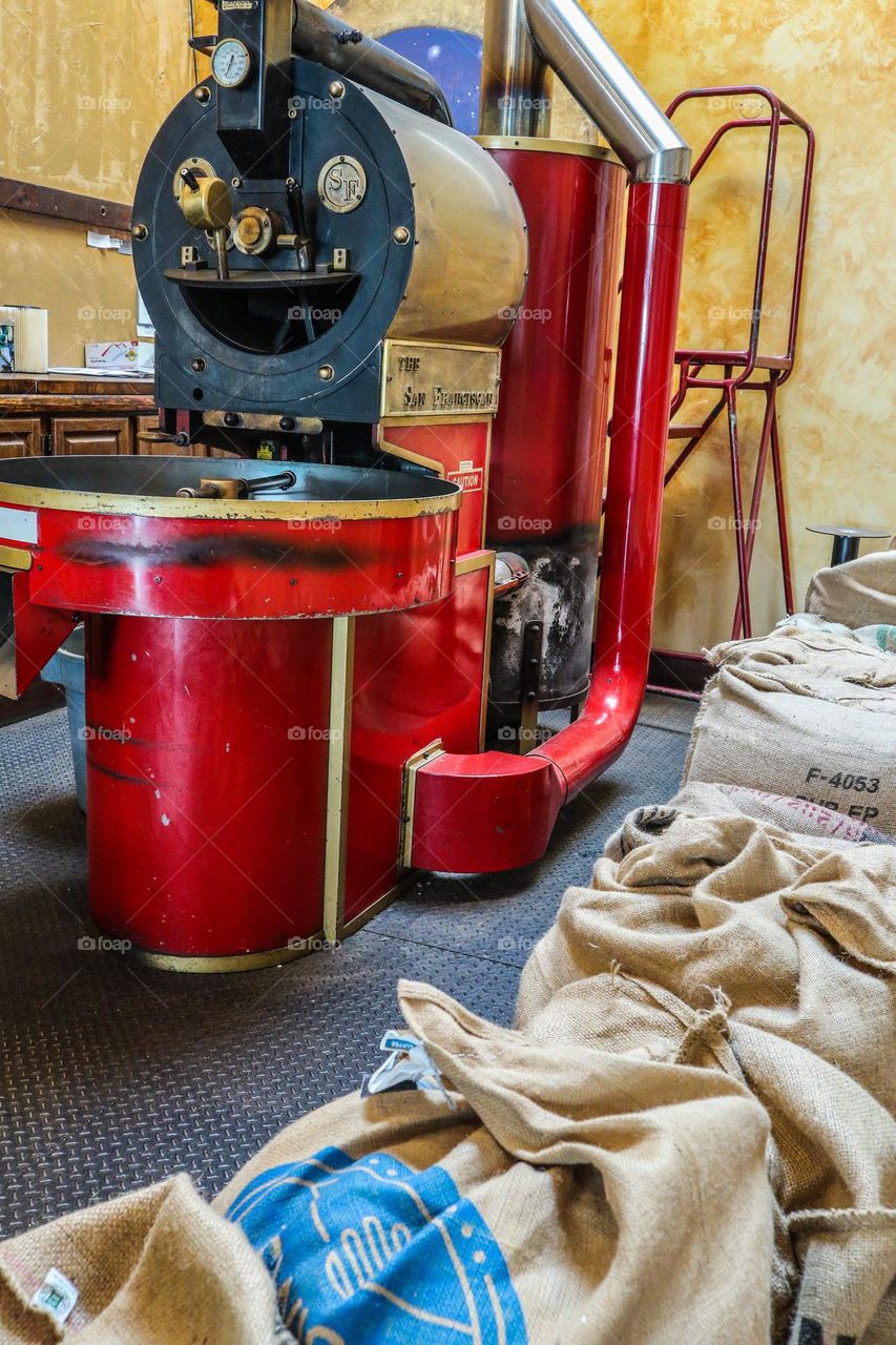 Big vintage red coffee roaster in a San Francisco coffee shop with sacks of fresh coffee beans ready to be roasted and enjoyed by customers
