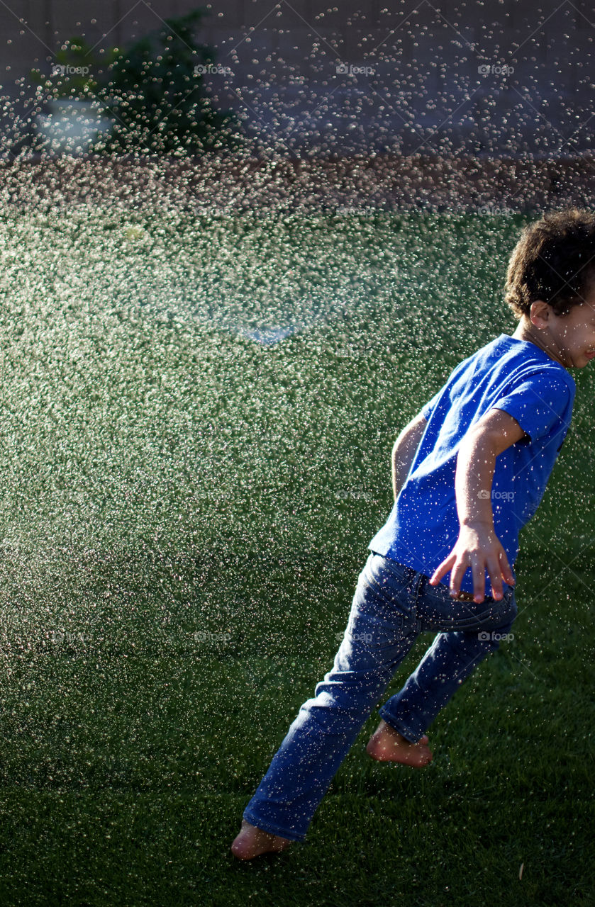 Boy playing in sprinklers 