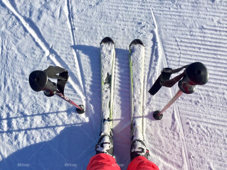 Looking down at feet wearing skis with ski poles beside
