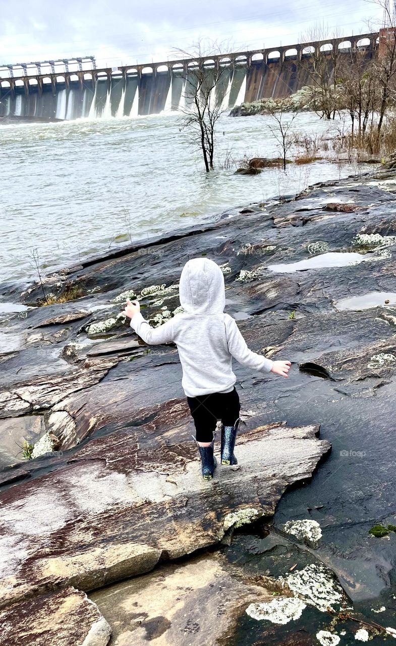 A child bravely steps across slippery rocks near the water. A depiction of childlike wonder and wanderlust 