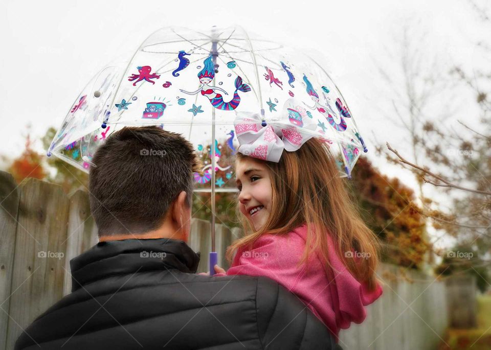 Daddy takes little daughter for a walk, prepared for fall showers with an umbrella.