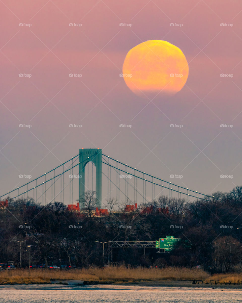 Huge full super moon rising above a long suspension bridge at dusk. 