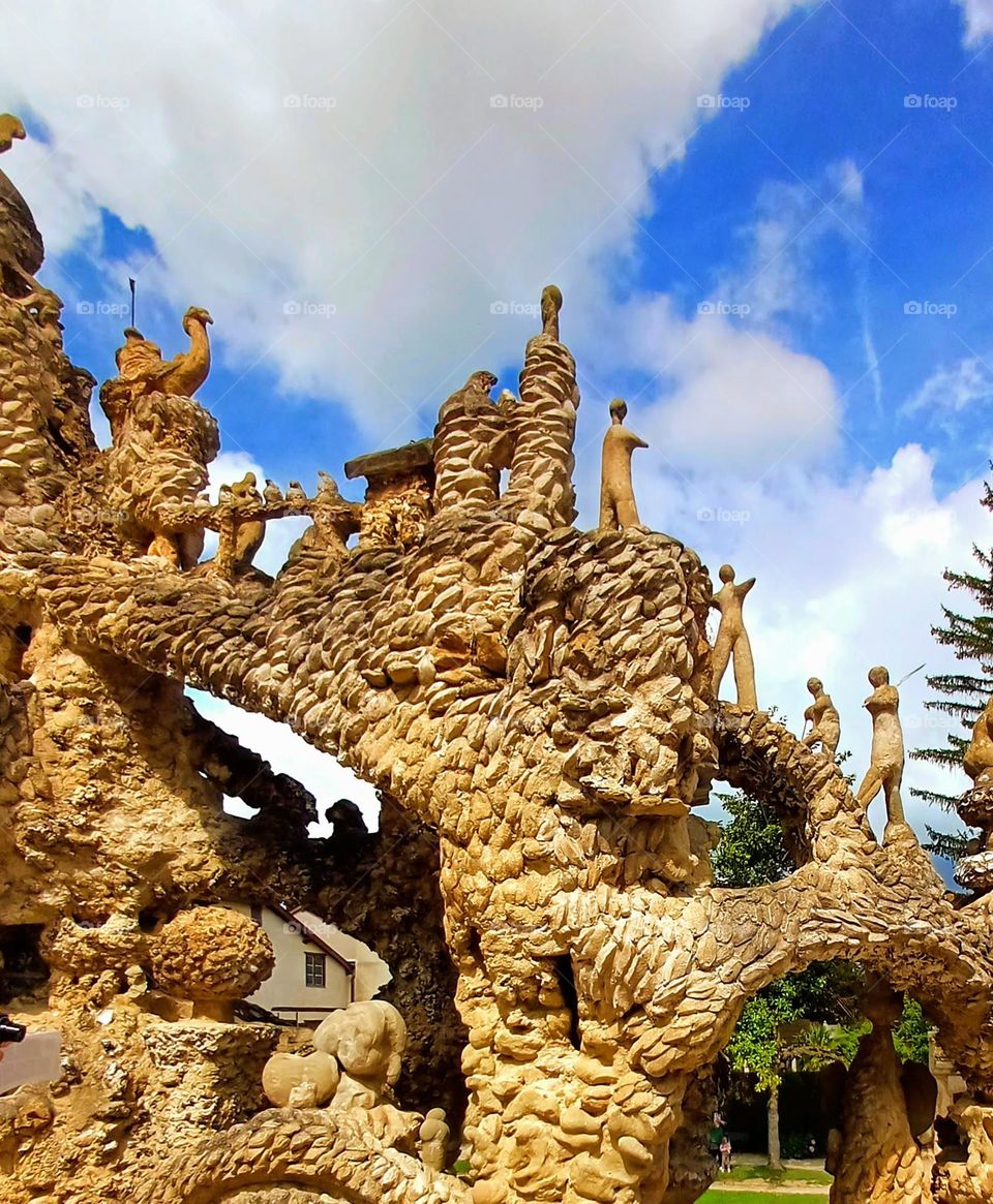 Section of the Palais Idéal du Facteur Cheval, showcasing its intricate and imaginative stonework. The structure is adorned with a variety of elaborate patterns and textures, resembling natural formations like twisted roots or vines.